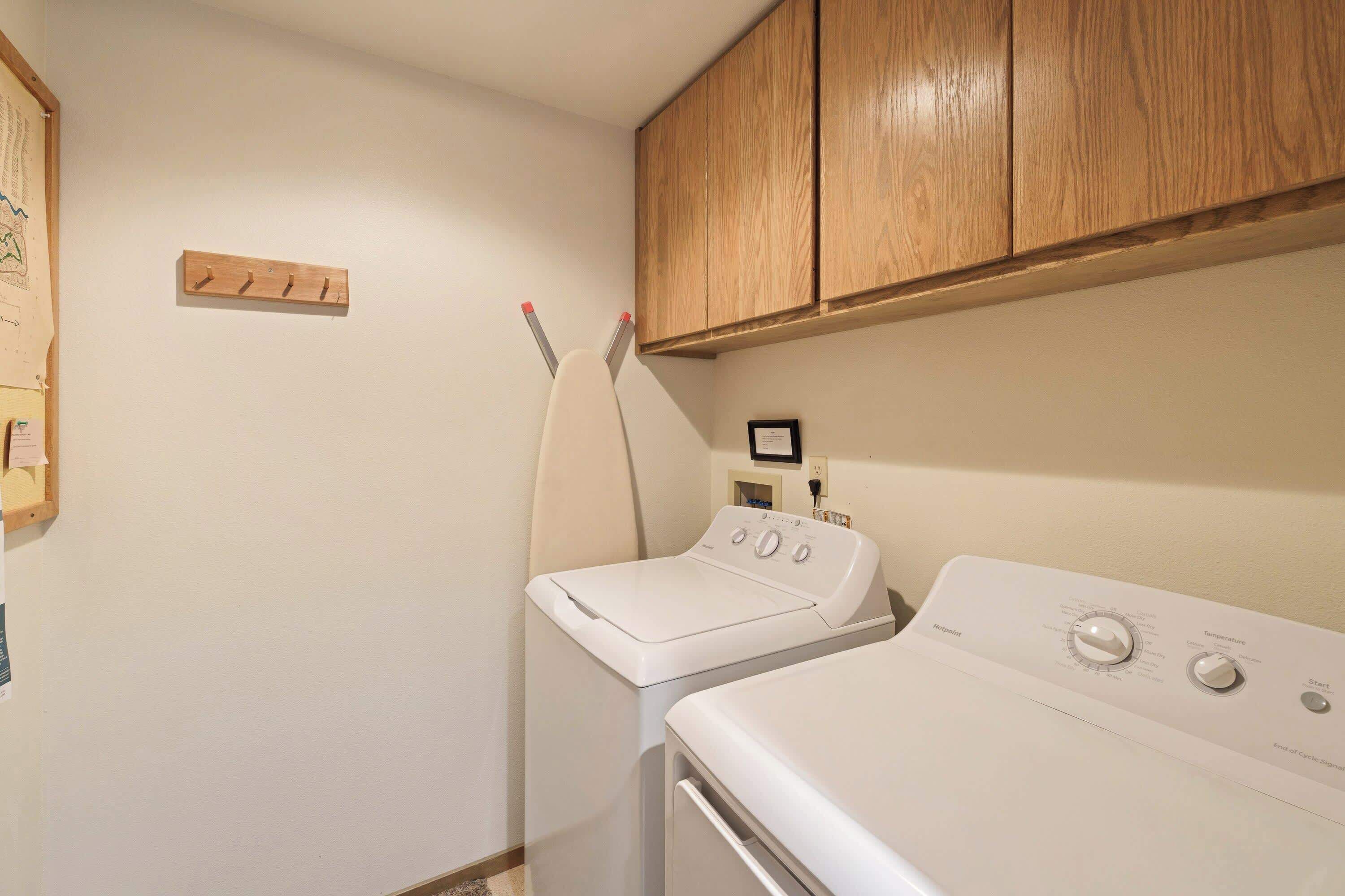 A laundry room with two white washing machines, wooden cabinets above, and a small wooden shelf with hooks.