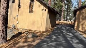 Eine Holzhütte mit der Nummer 13, umgeben von Kiefern und einer gepflasterten Auffahrt.