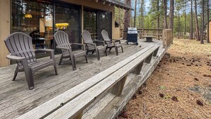 Eine Holzterrasse mit Adirondack-Stühlen, einem Grill und Blick auf ein bewaldetes Gebiet.