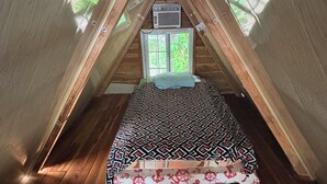 Une petite chambre mansardée avec un lit, une fenêtre et un appareil de climatisation.