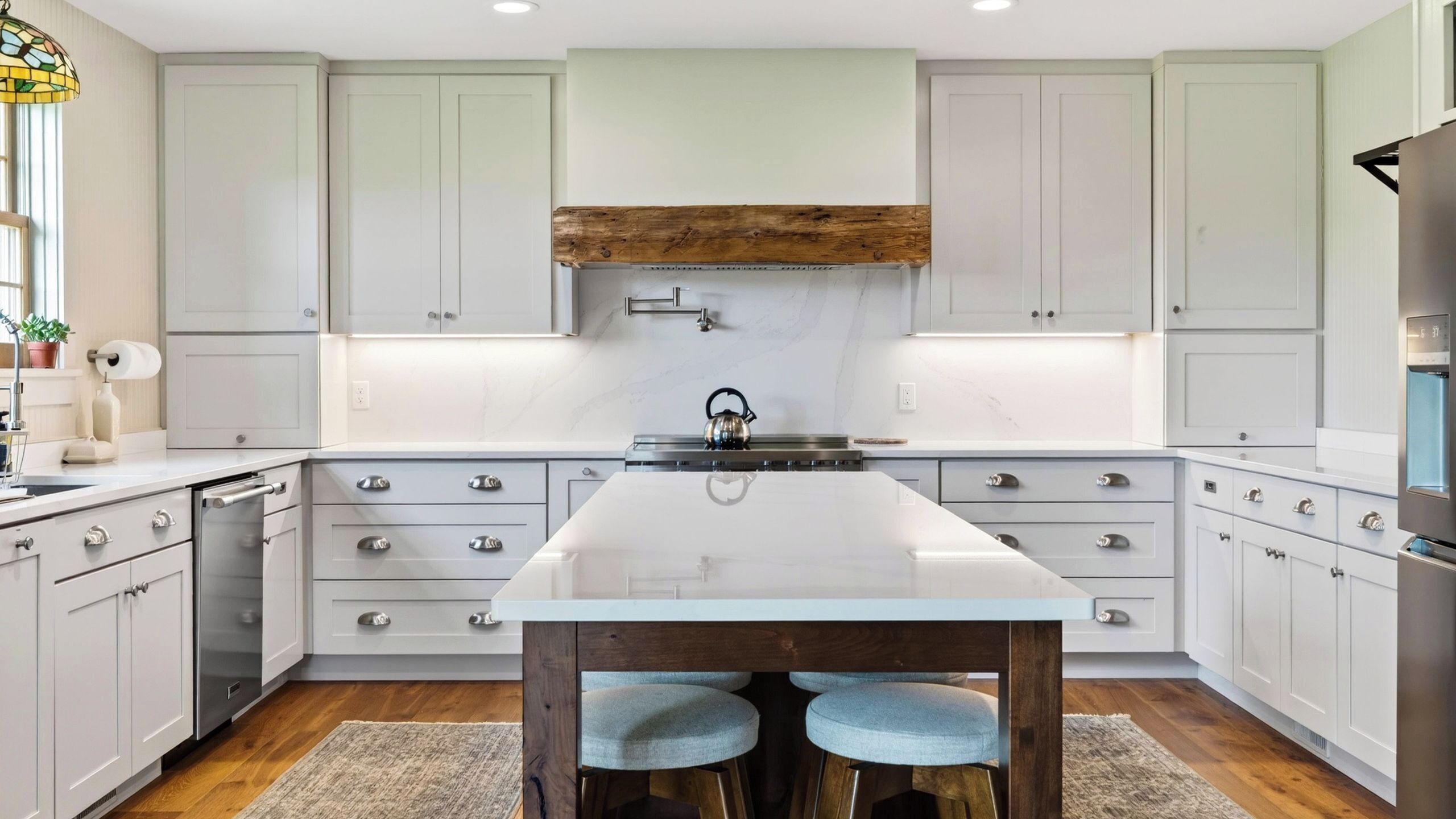 A modern kitchen with white cabinetry, a central island, and a wooden beam above the stove.