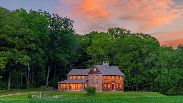 A two-story log cabin with a chimney, surrounded by a well-maintained lawn and dense forest. - 52-acre Berkshires Farmhouse Fire Pit, Outdoor Dining + Trails Copper Kettle Farm by Avantstay (Ashley Falls)