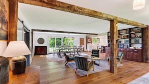 A spacious living area with a high ceiling, wooden beams, a dining set, and a bookshelf. - 52-acre Berkshires Farmhouse Fire Pit, Outdoor Dining + Trails Copper Kettle Farm by Avantstay (Ashley Falls)