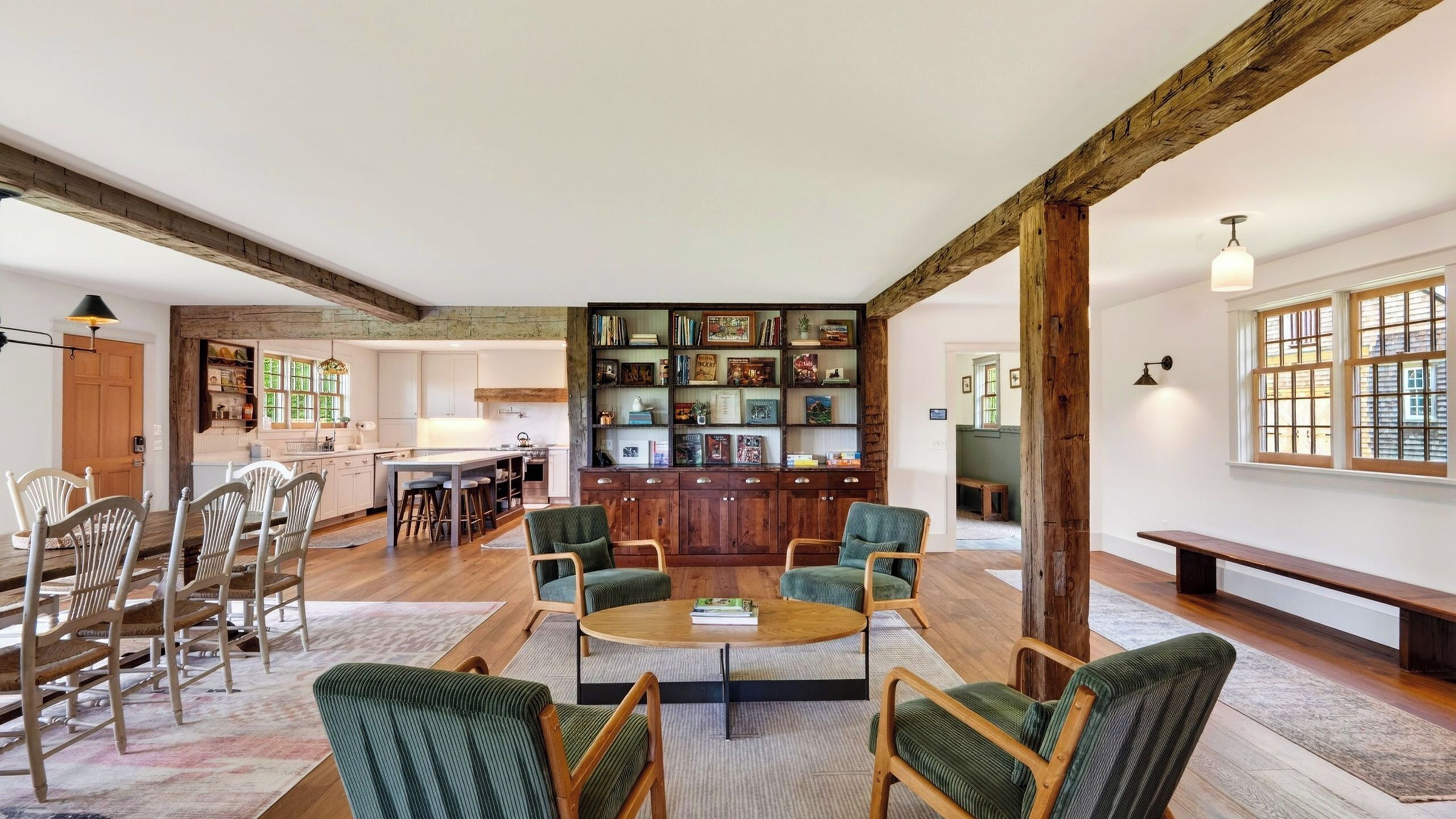 A spacious living area with a central coffee table, surrounded by green upholstered chairs, a wooden bench, and a bookshelf filled with books and decorative items.