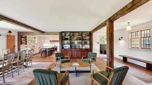 A spacious living area with a central coffee table, surrounded by green upholstered chairs, a wooden bench, and a bookshelf filled with books and decorative items. - 52-acre Berkshires Farmhouse Fire Pit, Outdoor Dining + Trails Copper Kettle Farm by Avantstay (Ashley Falls)