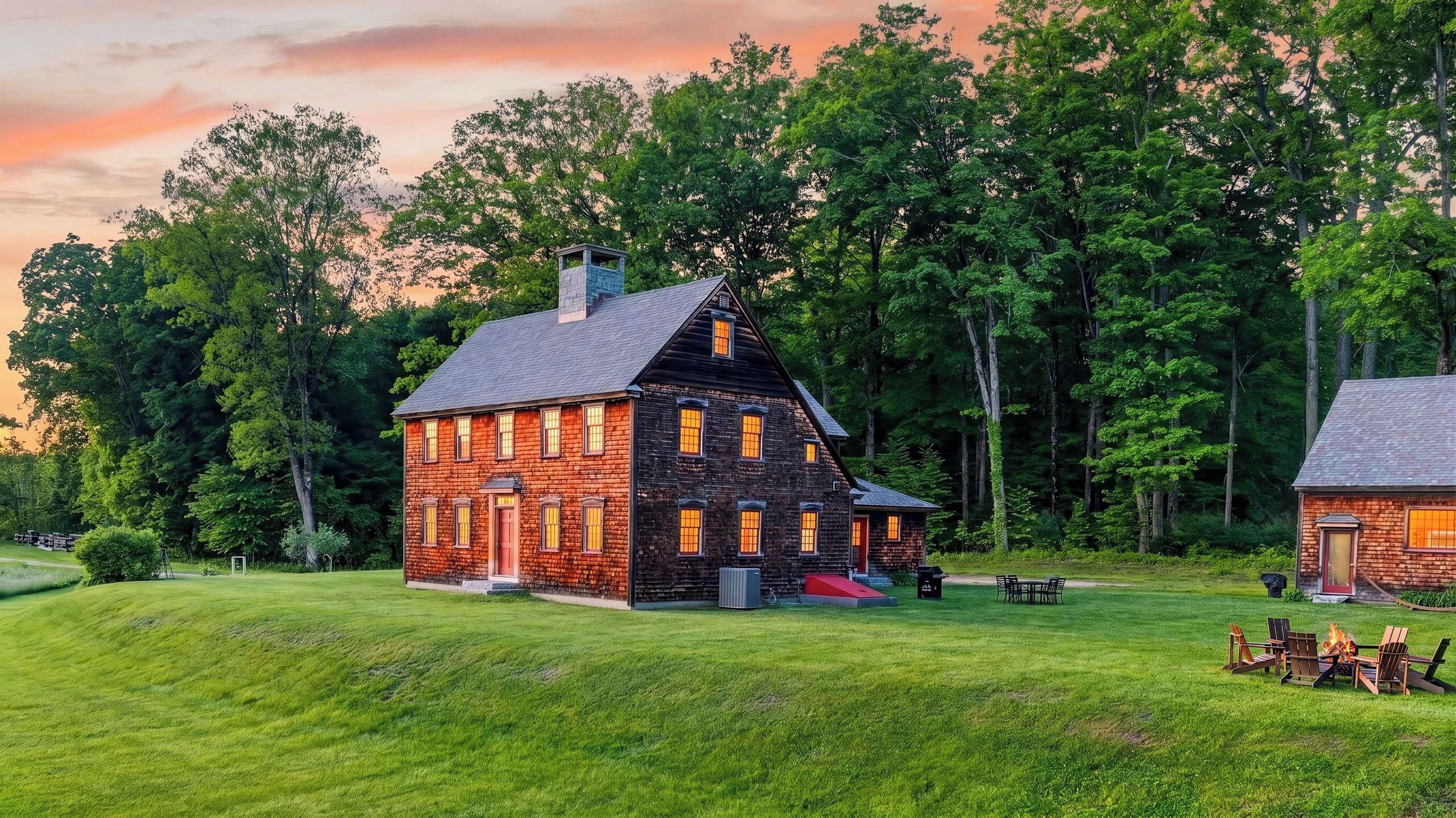 A two-story stone house with a large front porch, surrounded by a well-maintained lawn and dense trees.