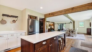 A modern kitchen with a central island, white cabinetry, and a stainless steel refrigerator. - 52-acre Berkshires Farmhouse Fire Pit, Outdoor Dining + Trails Copper Kettle Farm by Avantstay (Ashley Falls)