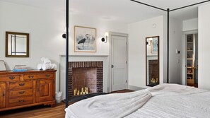 Um quarto com uma cama de dossel, uma cômoda de madeira, uma lareira e uma estante de livros.