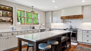 A modern kitchen with a large island, white cabinetry, and a view of greenery through the windows. - 52-acre Berkshires Farmhouse Fire Pit, Outdoor Dining + Trails Copper Kettle Farm by Avantstay (Ashley Falls)