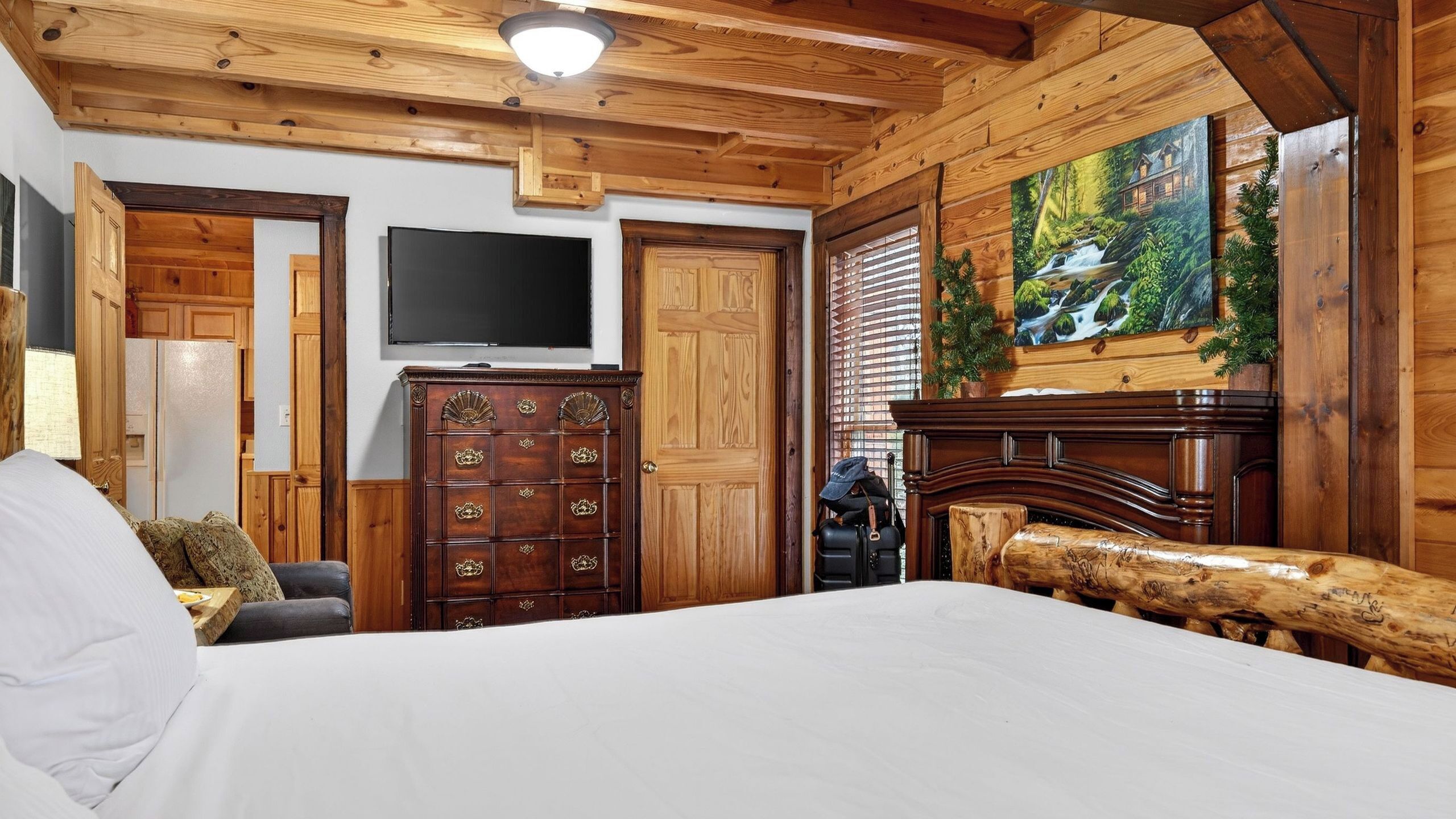 A wooden interior with a bed, a TV, a fireplace, and a painting of a waterfall.
