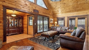 A log cabin interior with a wooden dining table, a leather sofa, and a patterned rug. - Hot Tub, Game Room & Prime Pigeon Forge Location Big Bear Ridge by Avantstay (Pigeon Forge)