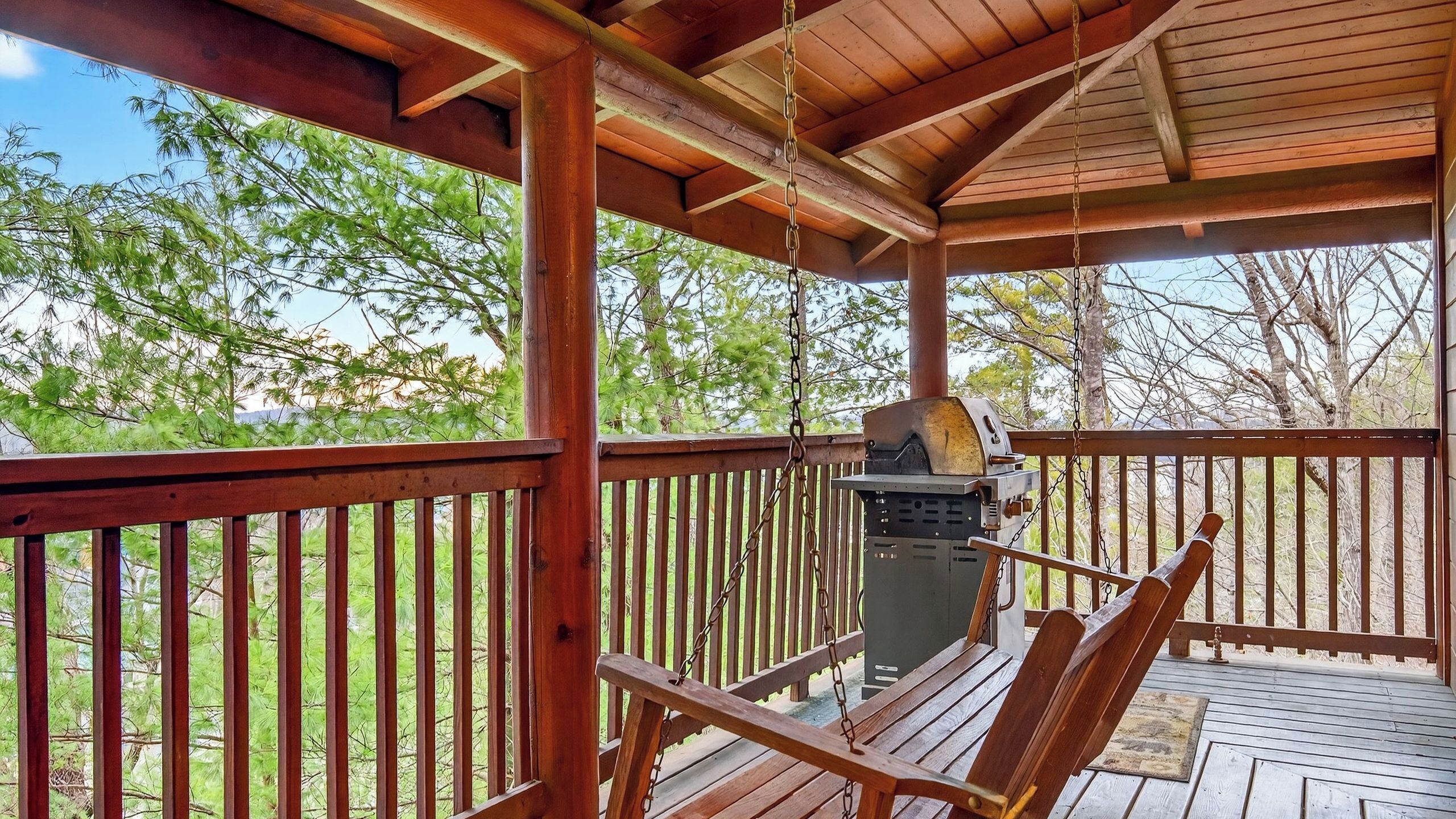A wooden deck with a grill and a swing chair.