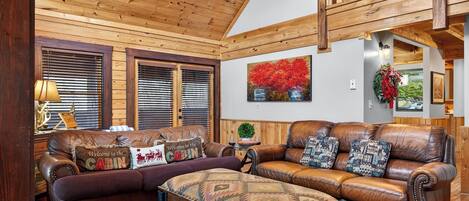 A cabin interior with a wooden ceiling, leather sofas, and a fireplace.