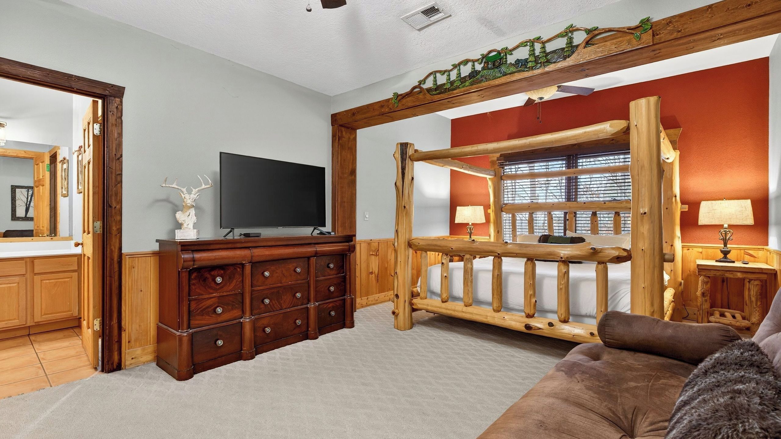 A room with a wooden bed frame, a television, a dresser, and a window with blinds.