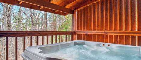 A hot tub in a wooden cabin with a view of trees.