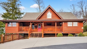 A log cabin with a front porch, a red door, and a small front yard.