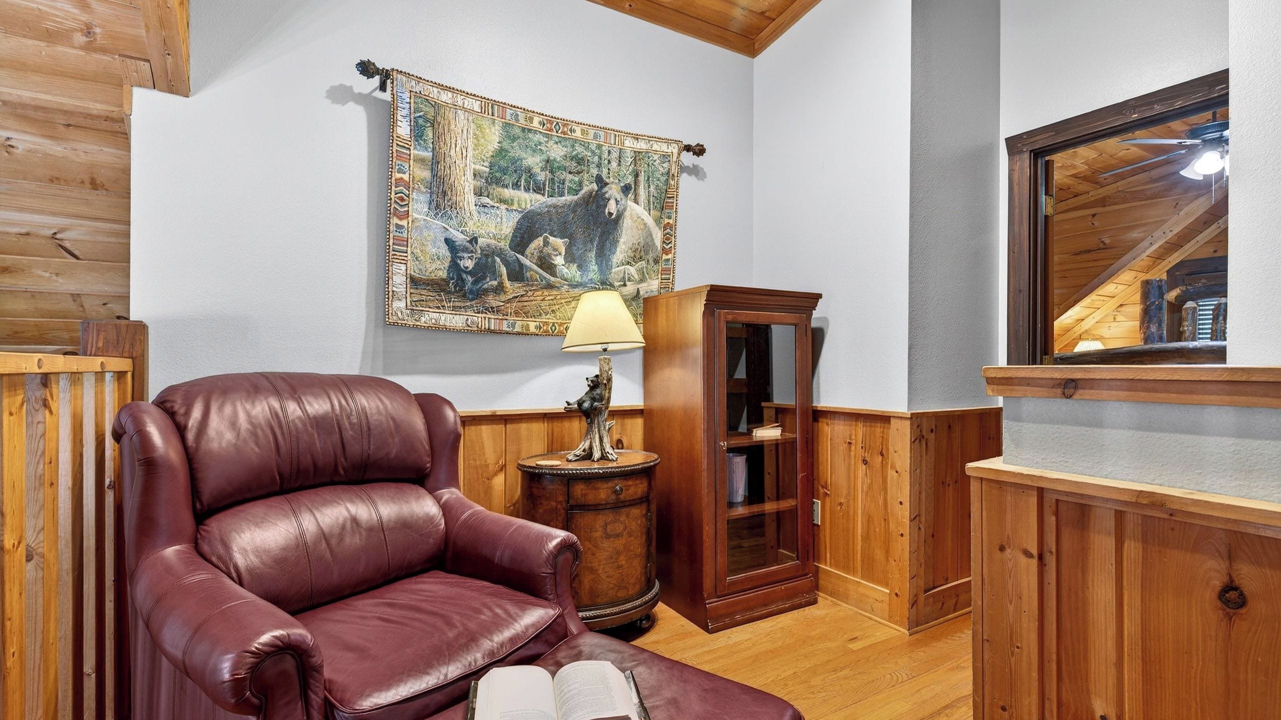 Una habitación con un sillón de cuero, un armario de madera, una lámpara y un tapiz en la pared.