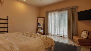 Een hotelkamer met een bed, een slaapbank, een plafondventilator, een aan de muur bevestigde televisie en een groot raam met gordijnen.