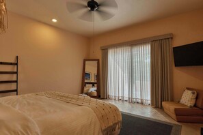 Ein Hotelzimmer mit einem Bett, einem Sofa, einem Deckenventilator, einem an der Wand montierten Fernseher und einem großen Fenster mit Vorhängen.
