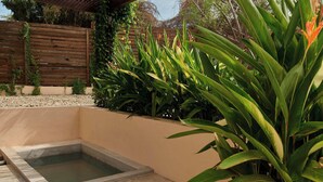 Een tuin met een klein zwembad, omringd door weelderige groene beplanting en een houten omheining.