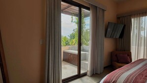 Een hotelkamer met een bed, een aan de muur bevestigde televisie en een balkon met uitzicht op groen.