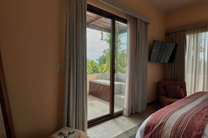 Ein Hotelzimmer mit Bett, Wandfernseher und Balkon mit Blick auf Grünflächen.