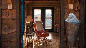 A wooden interior with a high ceiling, a cozy seating area with a chair and a table, and a large window providing natural light. - Take in the rustic, fairy tale vibe of this custom-made treehouse in the midst of towering white oaks. Recline in a rocking chair and watch the sunset over the mountains, or try your hand at some stargazing from the comfort of the deluxe double bed.< (Asheville)