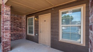 A building exterior with a brick column, a beige door, and two windows with blinds. - Spacious 2 Bed - Floor 1 - Reserved Parking (Oklahoma City)
