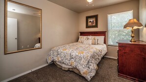 A bedroom with a large mirror, a bed with floral bedding, a ceiling fan, a window with blinds, and a wooden dresser. - Spacious 2 Bed - Floor 1 - Reserved Parking (Oklahoma City)