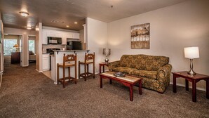 A living room with a sofa, two chairs, a coffee table, and a lamp. There is a kitchen in the background with cabinets and appliances. - Spacious 2 Bed - Floor 1 - Reserved Parking (Oklahoma City)