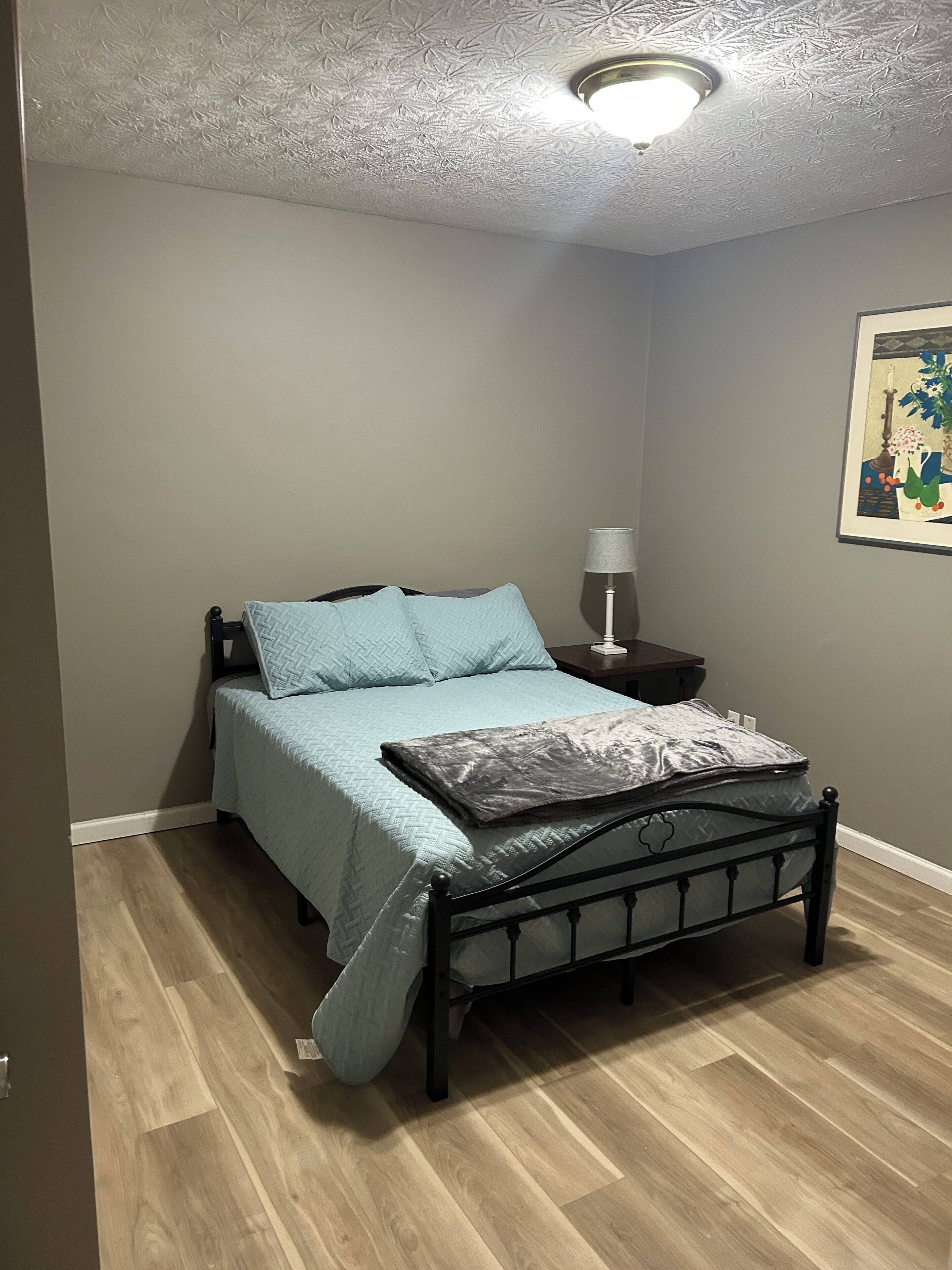 A bedroom with a bed, a nightstand, a lamp, and a painting on the wall.