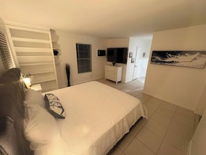 Un dormitorio con cama, armario, televisión y un cuadro en la pared.