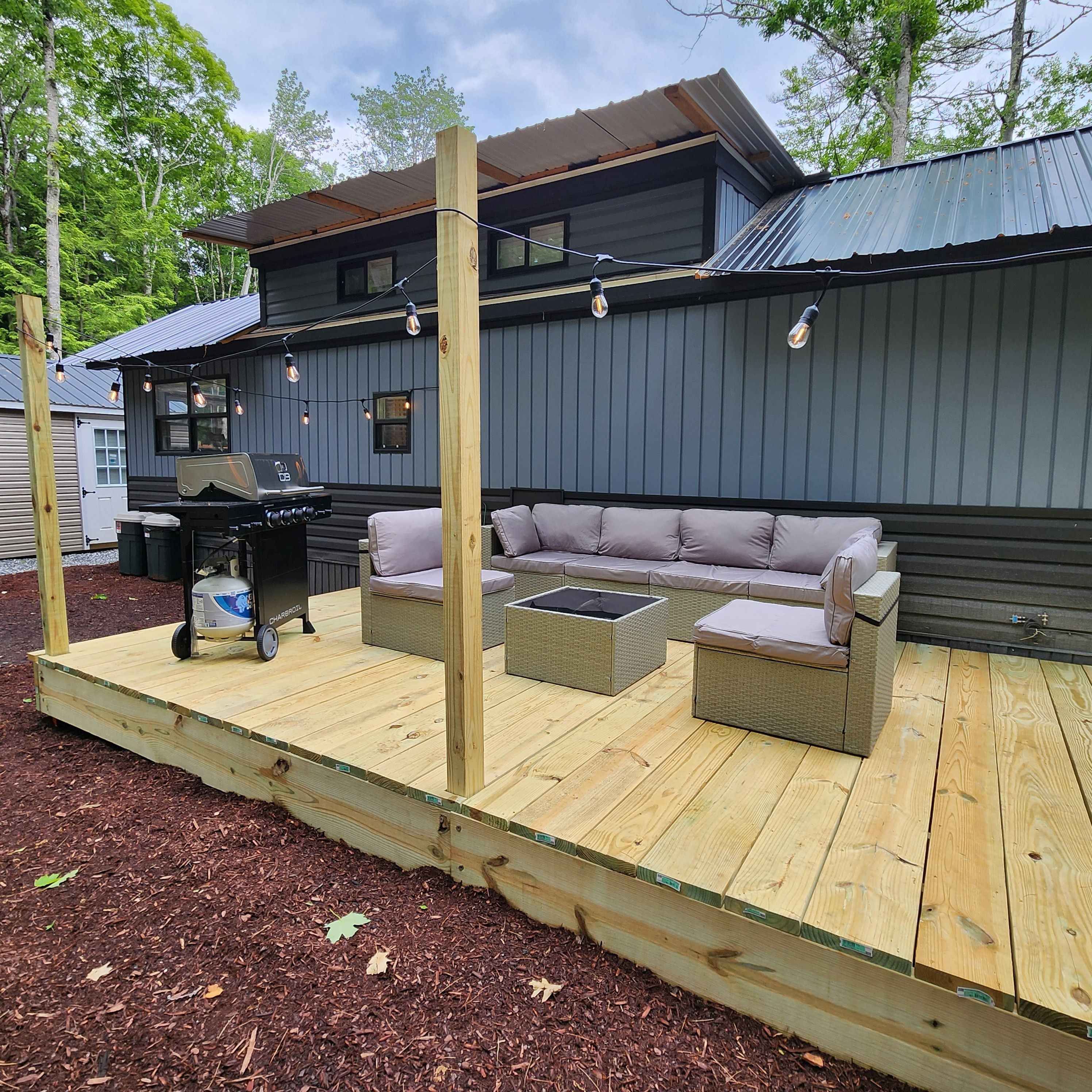 An outdoor patio area with a wooden deck, a barbecue grill, and a seating arrangement.