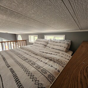 Ein Schlafzimmer mit einem Bett, zwei Fenstern, einer Holzreling und einer strukturierten Decke.