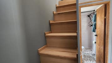 En trätrappa leder upp till ett rum med en vit kakelbeklädd vägg och en dörr med en handdukshängare.