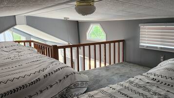 A bedroom with a sloped ceiling, a window with a view, a wooden railing, and patterned bedding.