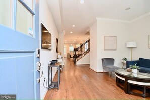 A spacious living area with hardwood flooring, a staircase, a blue sofa, a round coffee table, and a grey armchair. - Spacious 5BR Home Near Capitol Hill | Free Parking (Washington DC)