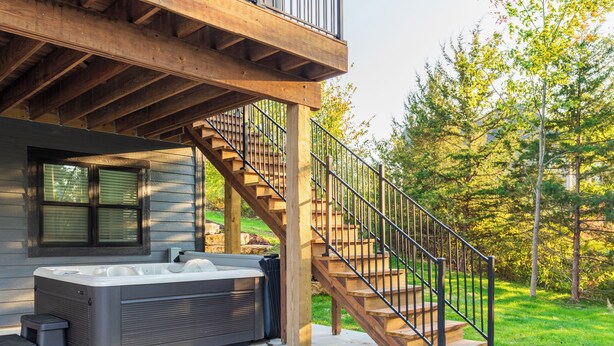 A hot tub outside a wooden house with a staircase leading up to a balcony. - New construction, Hot tub, Game room, Extra-large patio, Firepit, covered porch (Galena)