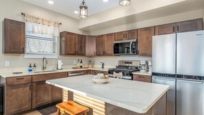 A modern kitchen with wooden cabinets, stainless steel appliances, and a marble island. - New construction, Hot tub, Game room, Extra-large patio, Firepit, covered porch (Galena)