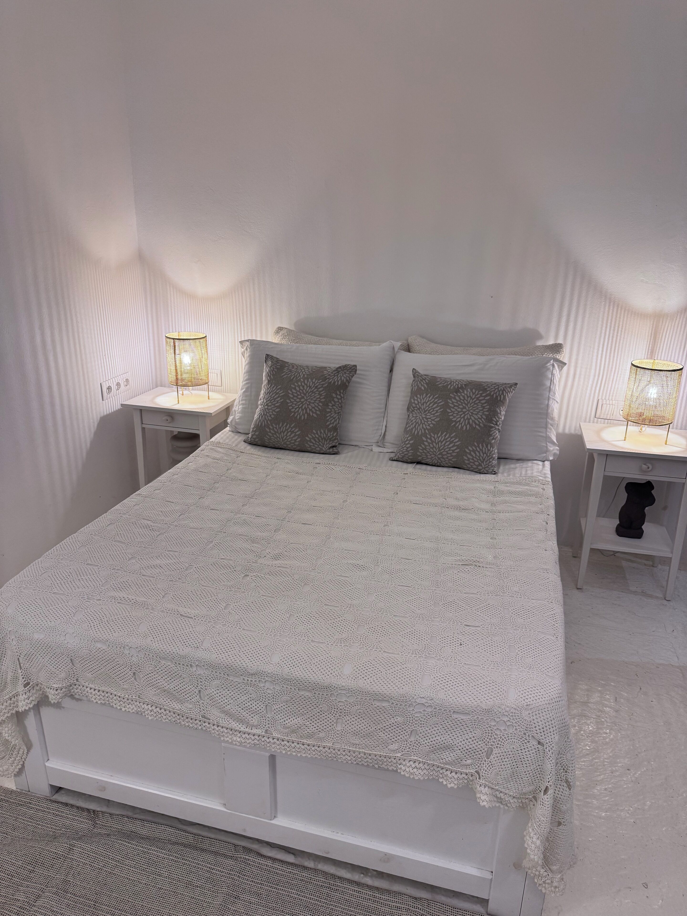 Un lit bien fait, recouvert d’une courtepointe blanche et agrémenté de deux oreillers, avec deux tables de chevet de chaque côté, sur lesquelles sont posées des lampes.