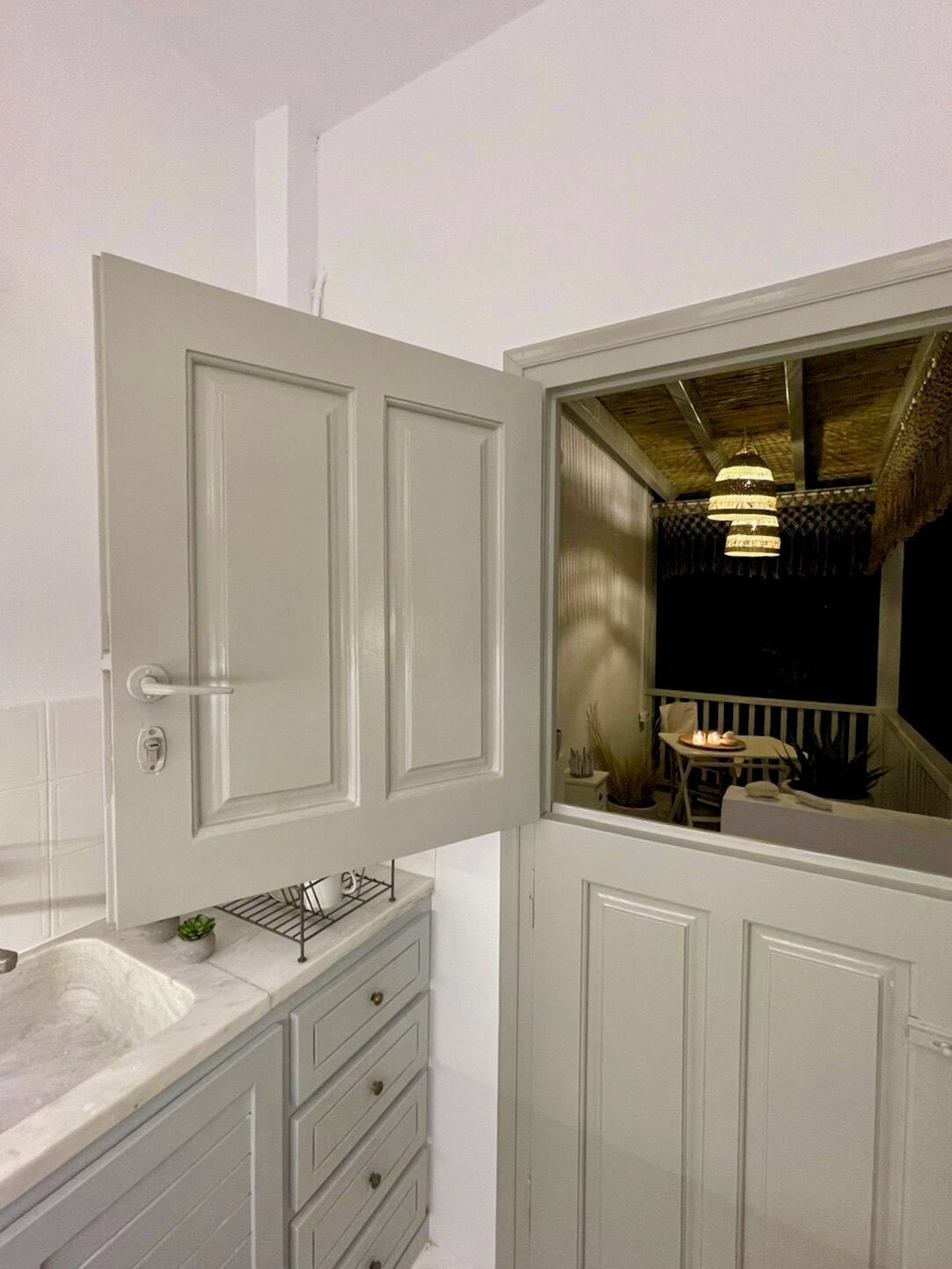 A bathroom with a white vanity, a bathtub, and a door leading to an outdoor area with a thatched roof and hanging lights.
