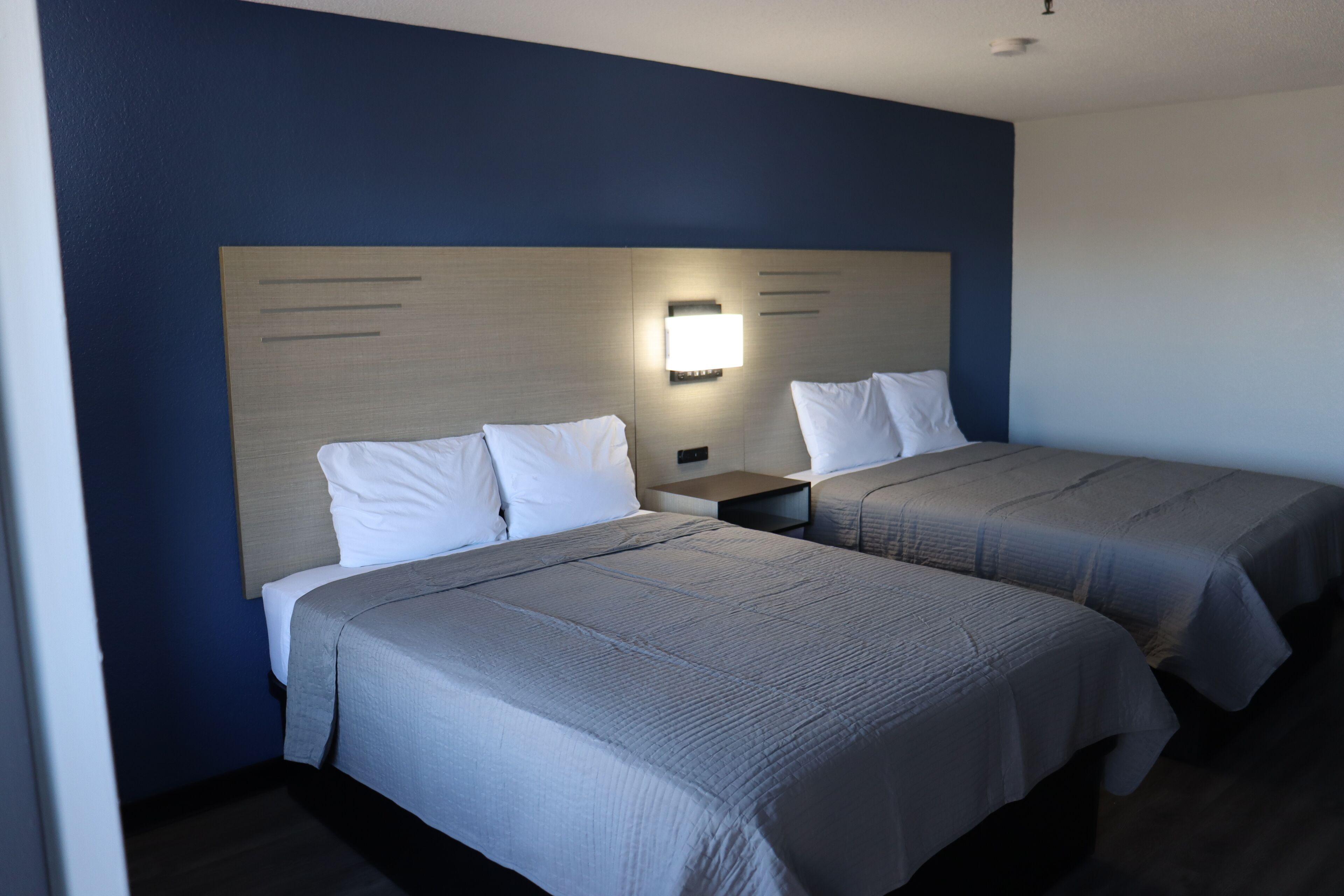 Una habitación de hotel con dos camas, una mesita de noche y una lámpara fijada a la pared.