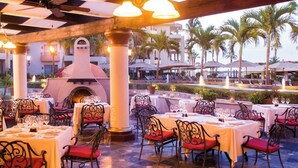 An outdoor dining area with tables and chairs, a central fire feature, and a view of a pool and palm trees. - Endless Ocean Views, Beautiful Blend of indoor, outdoor space. July Aug specials (Cabo San Lucas)