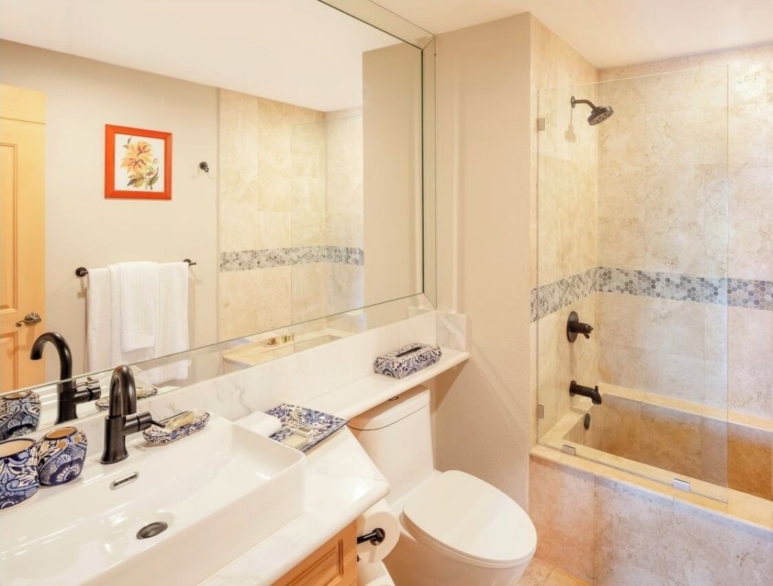 A modern bathroom with a large mirror, a white sink, a toilet, and a glass-enclosed shower.