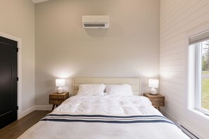A bedroom with a bed, bedside lamps, a window, and an air conditioning unit.