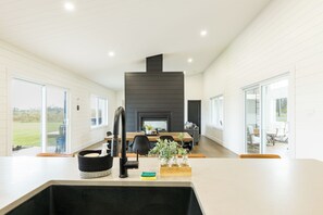 A modern kitchen with a central island, a dining area with a fireplace, and large windows offering views of the outdoors.