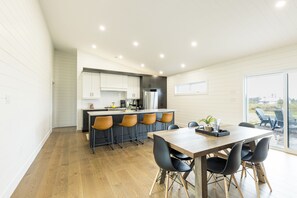 A modern kitchen with a central island, bar stools, and a dining table with chairs. - Waves and Woods Vacation Rental (Lot 39)