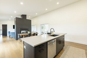 A modern kitchen with a large island, dark cabinetry, and a built-in dishwasher. - Waves and Woods Vacation Rental (Lot 39)
