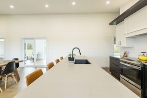 A modern kitchen with a central island, a dining area with chairs, and a view of the outdoors through a sliding door.