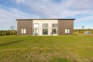 A modern two-story building with a flat roof, large windows, and a grassy lawn in front. - Waves and Woods Vacation Rental (Lot 39)
